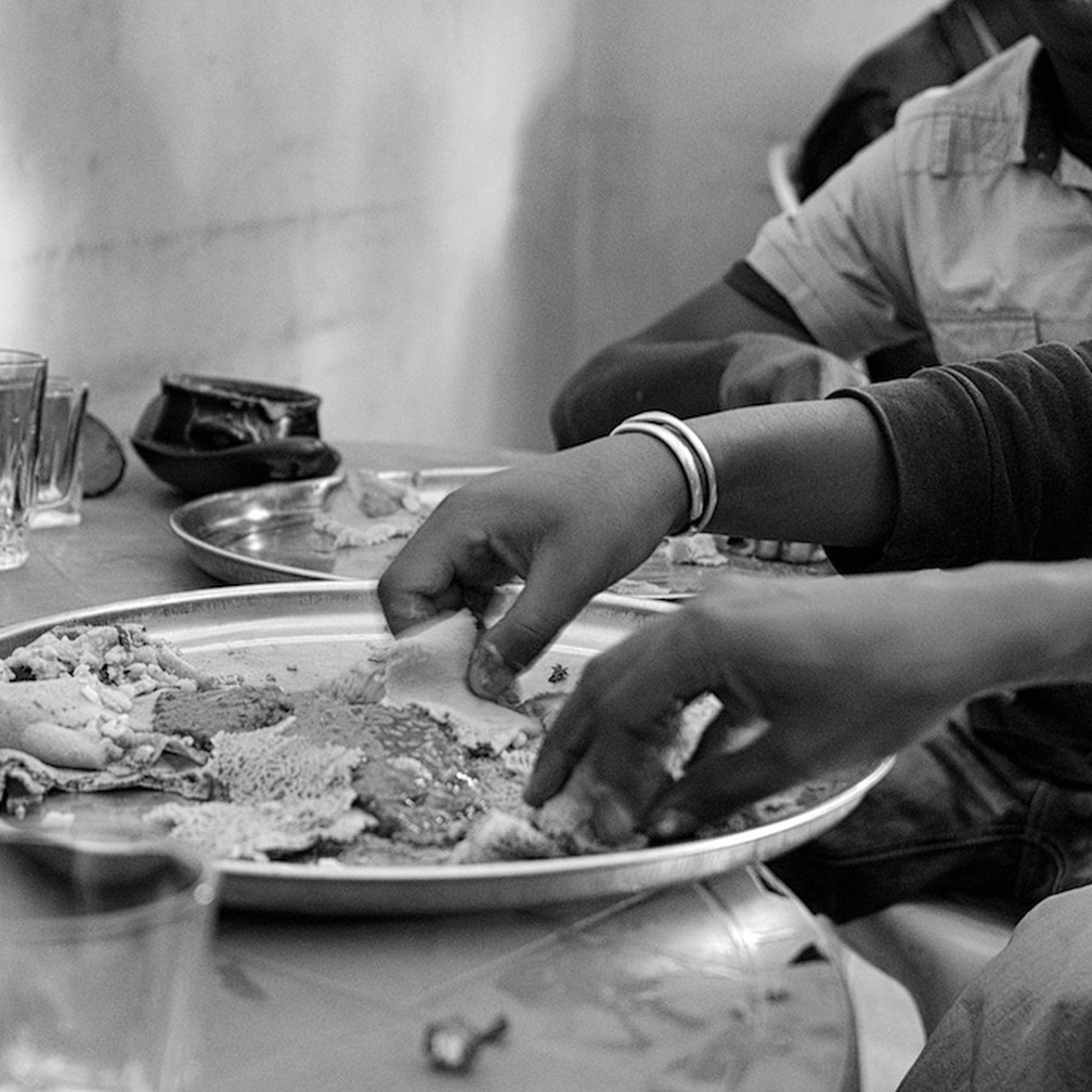 Hands sharing injera and stews from one communal platter